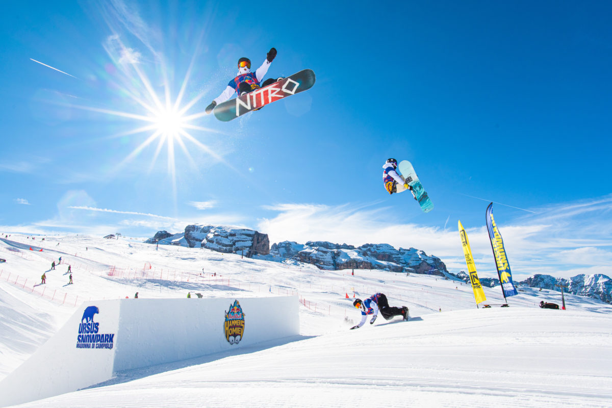 Snowboarders jumping over a kicker in Madonna di Campiglio